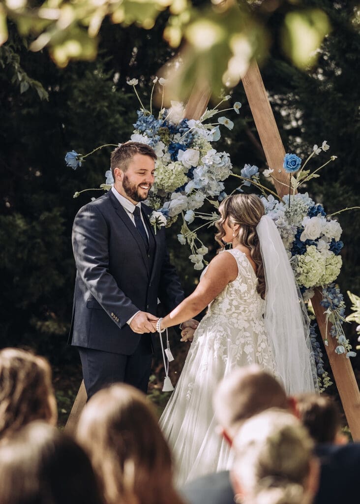 Bride and groom exchanging vows during outdoor ceremony at Vanden Estate Mildura with blue floral arch, photographed by Miss Moody Photography