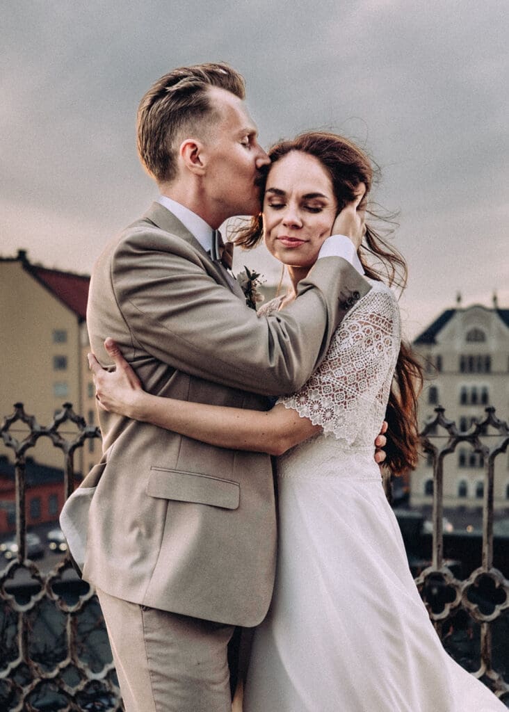 Groom kissing bride on forehead during sunset wedding portraits outside Uspenski Cathedral Helsinki, moody cinematic wedding photography, Miss Moody Photography — Sulhanen suutelee morsianta otsalle auringonlaskun häämuotokuvien aikana Uspenskin katedraalin ulkopuolella Helsingissä, tunnelmallinen elokuvallinen hääkuvaus, Miss Moody Photography