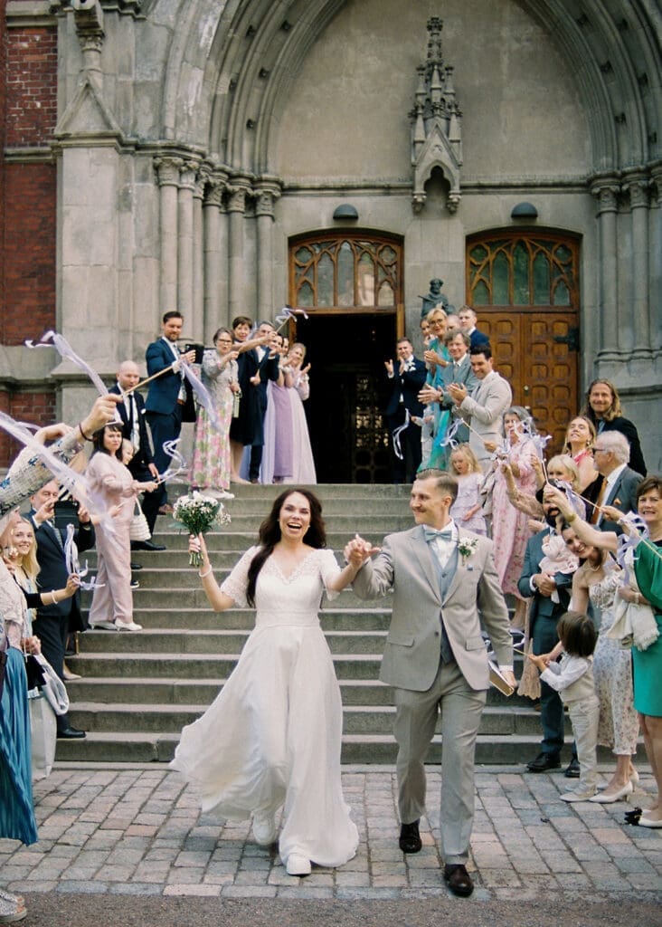 Bride and groom confetti exit outside Johanneksenkirkko Helsinki, joyful wedding celebration on church steps, Miss Moody Photography — Morsian ja sulhanen konfettipoistumiset Johanneksenkirkon ulkopuolella Helsingissä, iloinen häätapahtuma kirkon portailla, Miss Moody Photography