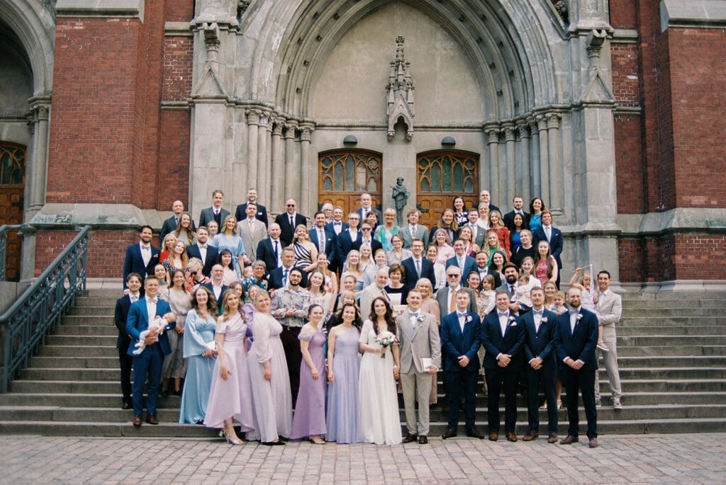 Wedding group photo outside Johanneksenkirkko church Helsinki, full wedding party on church steps, Miss Moody Photography — Häiden ryhmäkuva Johanneksenkirkon ulkopuolella Helsingissä, koko hääseurue kirkon portailla, Miss Moody Photography