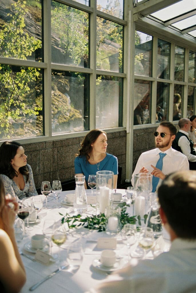 Wedding guests seated at reception table Ravintola Sipuli Helsinki, candid moment during speeches, film photography, Miss Moody Photography — Häävieraat istuvat vastaanottoruudulla Ravintola Sipulissa Helsingissä, aito hetki puheiden aikana, filmivalokuvaus, Miss Moody Photography