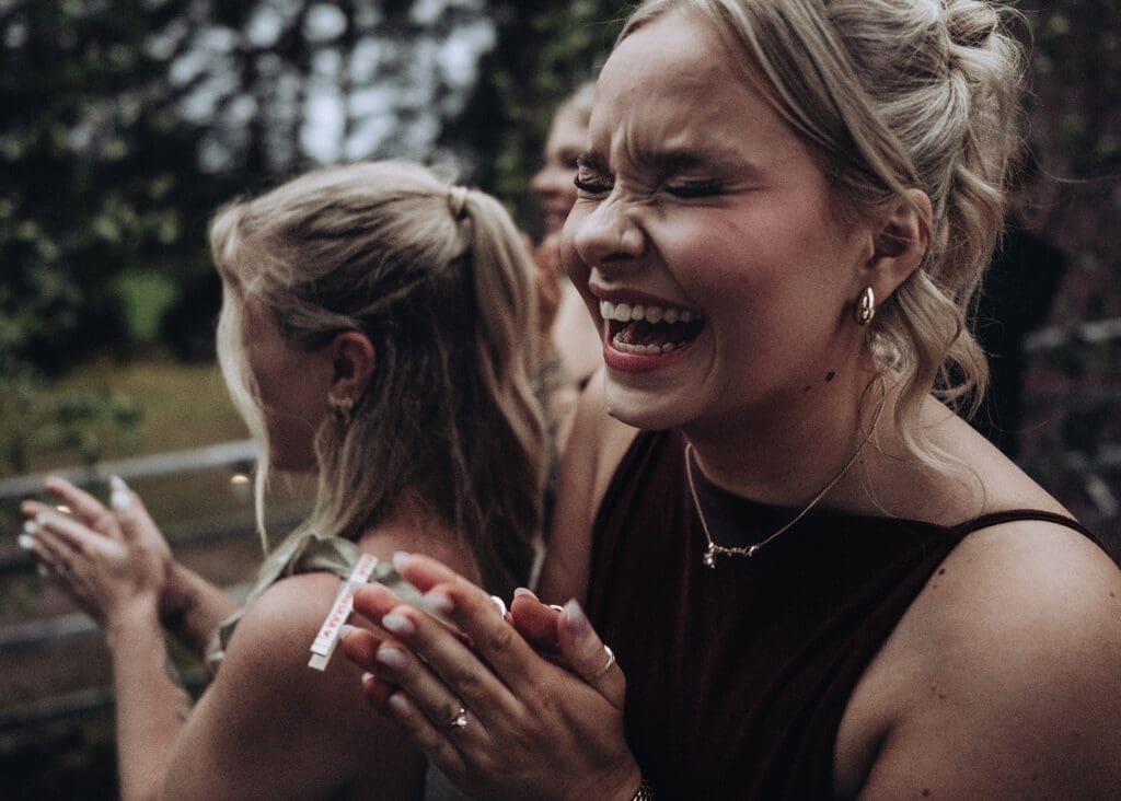 Wedding guest laughing with joy during bouquet throw at Aurantola wedding reception in Jaala Kymenlaakso Finland, moody documentary wedding photography by Miss Moody Photography | Häävieraalla iloinen nauru kukkaheiton aikana Aurantolan häissä Jaalassa Kymenlaaksossa, tunnelmallinen hääkuvaus Miss Moody Photography
