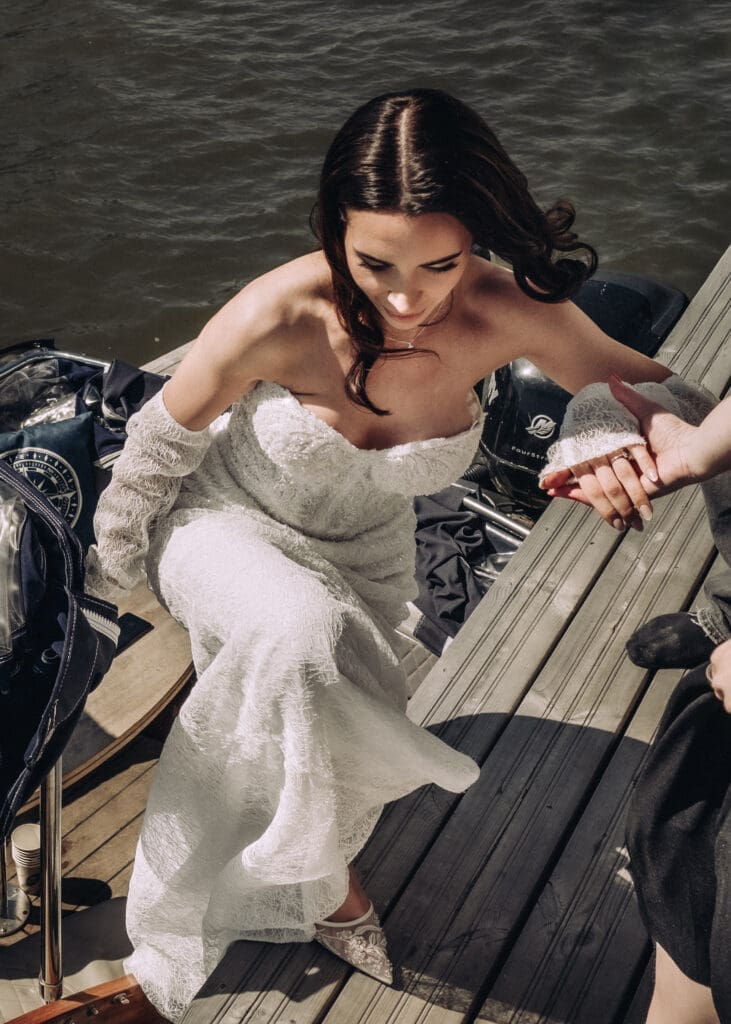 Bride stepping off private boat onto dock arriving at Kulosaari Casino Helsinki wedding, lace wedding dress, candid arrival moment, Miss Moody Photography — Morsian astuu yksityisveneestä laiturille saapuessaan Kulosaaren Casinolle Helsingissä häissä, pitsinen hääpuku, aito saapumishetki, Miss Moody Photography
