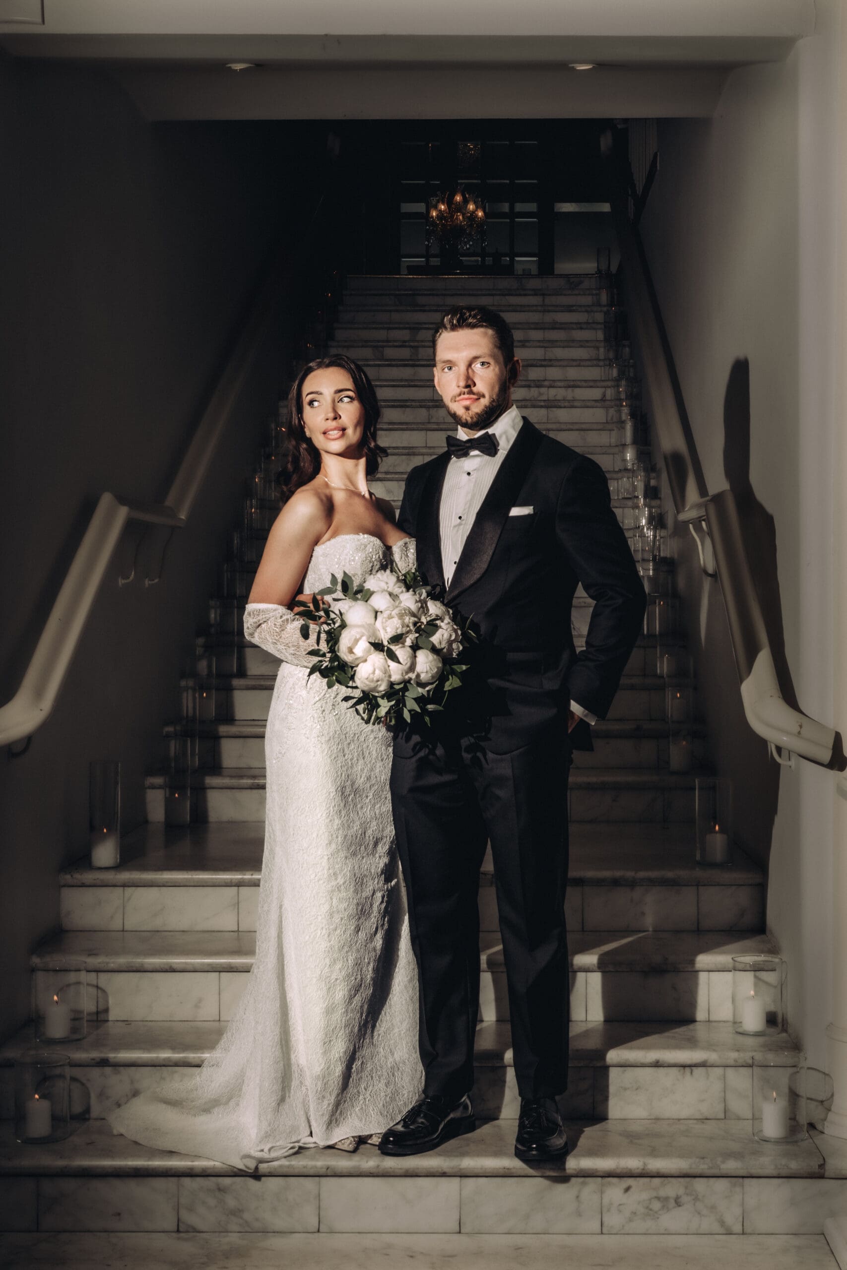 Bride and groom portrait on marble staircase at Kulosaari Casino Helsinki wedding, candles lining the steps, crystal chandelier above, moody editorial wedding photography, Miss Moody Photography — Morsiamen ja sulhasen muotokuva marmorisilla portailla Kulosaaren Casinolla Helsingissä häissä, kynttilät portaiden reunoilla, kristallikruunu yläpuolella, tunnelmallinen editoraalinen hääkuvaus, Miss Moody Photography