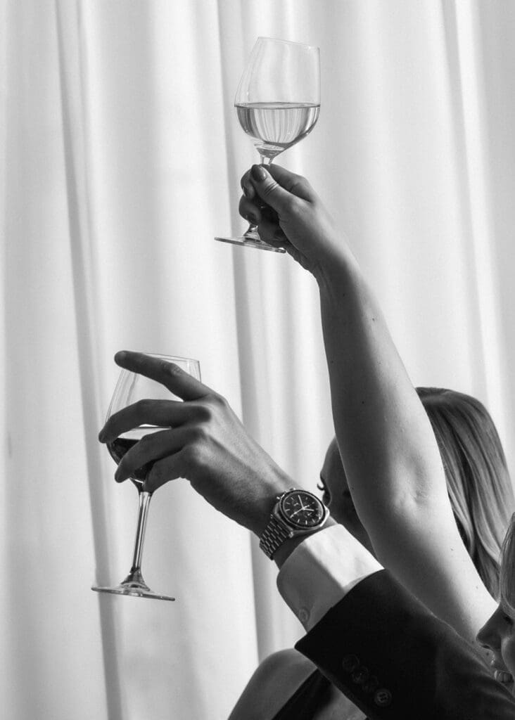 Bride and groom raising wine glasses in toast at Kulosaari Casino Helsinki wedding reception, black and white detail shot, luxury watch visible, Miss Moody Photography — Morsian ja sulhanen kohottavat viinilasit maljassa Kulosaaren Casinon häävastaanottolla Helsingissä, mustavalkoinen yksityiskohta, luksuskello näkyvissä, Miss Moody Photography