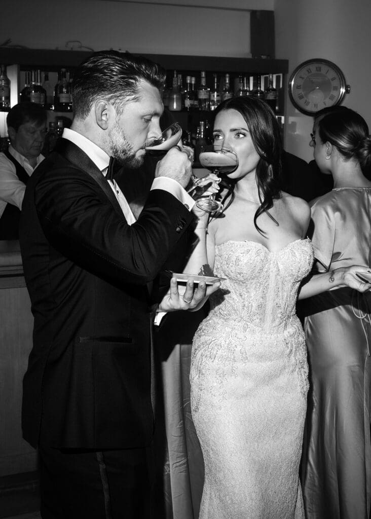 Bride and groom drinking espresso martinis together at bar during Kulosaari Casino Helsinki wedding reception, black and white candid wedding photography, Miss Moody Photography — Morsian ja sulhasen juovat espresso martineita yhdessä baarissa Kulosaaren Casinon häävastaanoton aikana Helsingissä, mustavalkoinen aito hääkuvaus, Miss Moody Photography