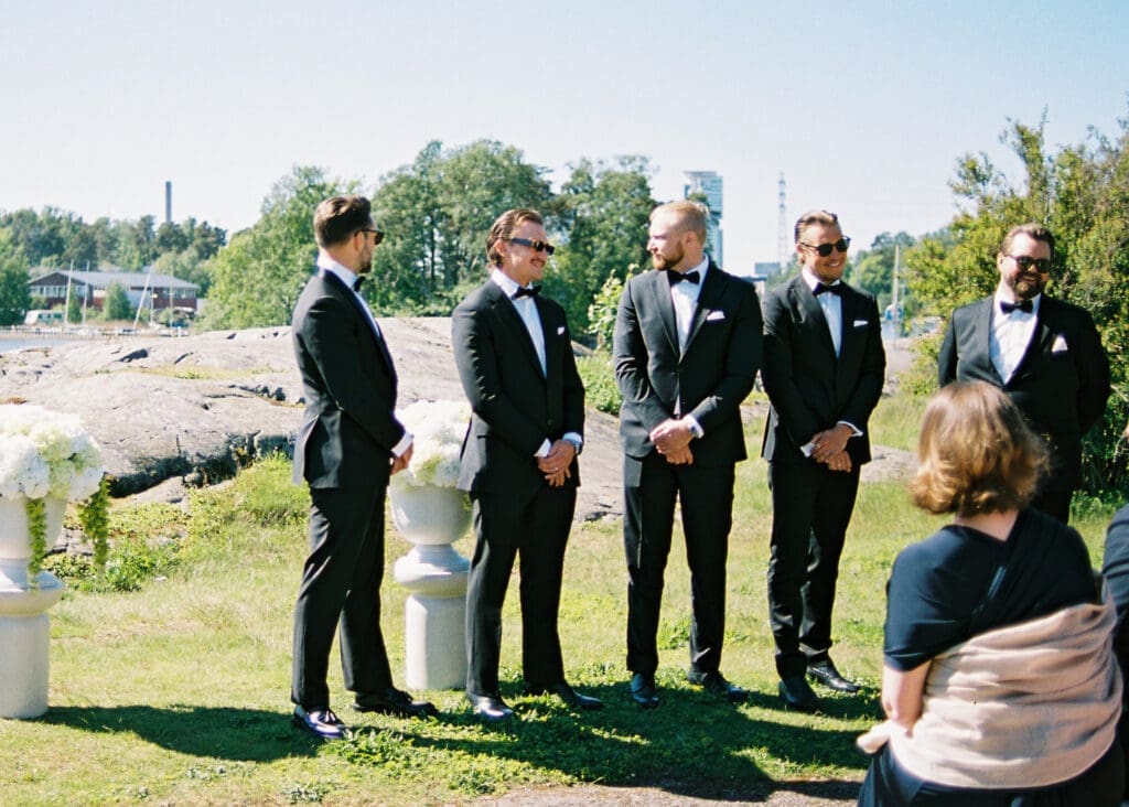 Groomsmen in black tuxedos waiting for ceremony on Helsinki archipelago rocks Kulosaari Casino, film photography, Miss Moody Photography — Sulhasen kaverit mustissa smokingeissa odottavat seremoniaa Helsingin saariston kalliolla Kulosaaren Casino, filmivalokuvaus, Miss Moody Photography