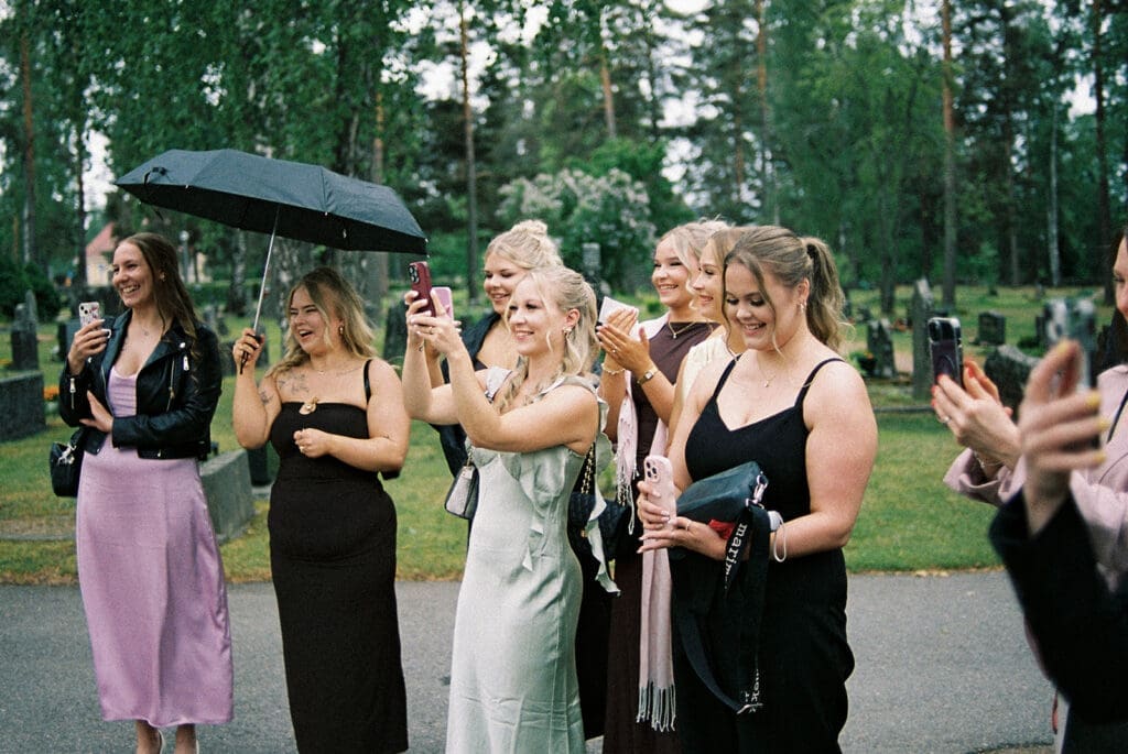 Wedding guests celebrating with umbrellas in the rain outside Valkeala kirkko Finland, moody documentary wedding photography Miss Moody Photography | Häävieraat sateessa Valkealan kirkon ulkopuolella, tunnelmallinen hääkuvaus Miss Moody Photography
