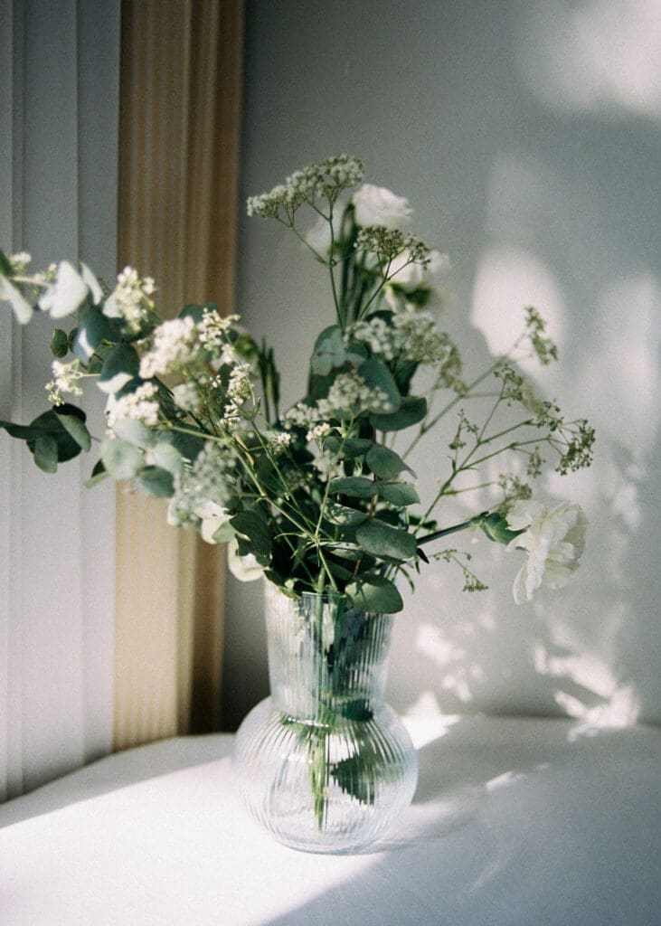 Wedding floral arrangement in ribbed glass vase with dappled shadow on wall Kulosaari Casino Helsinki, film photography, Miss Moody Photography — Häiden kukka-asetelma uurretussa lasimaljassa varjokuvioineen seinällä Kulosaaren Casinolla Helsingissä, filmivalokuvaus, Miss Moody Photography