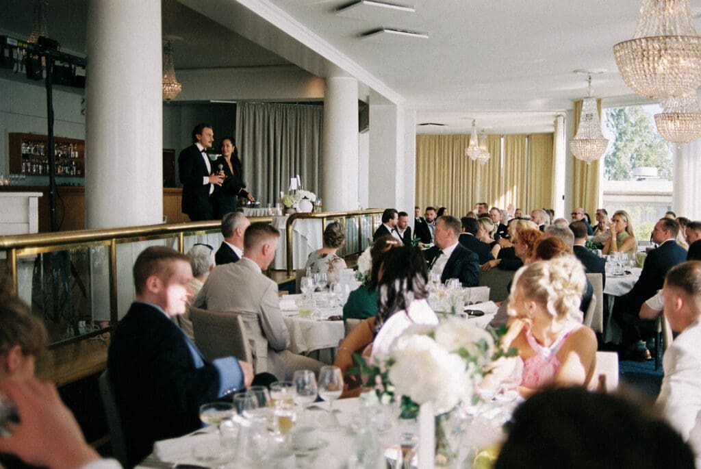 Wedding speeches during reception at Kulosaari Casino Helsinki, guests listening at tables, film photography, Miss Moody Photography — Hääpuheet vastaanoton aikana Kulosaaren Casinolla Helsingissä, vieraat kuuntelevat pöydissä, filmivalokuvaus, Miss Moody Photography