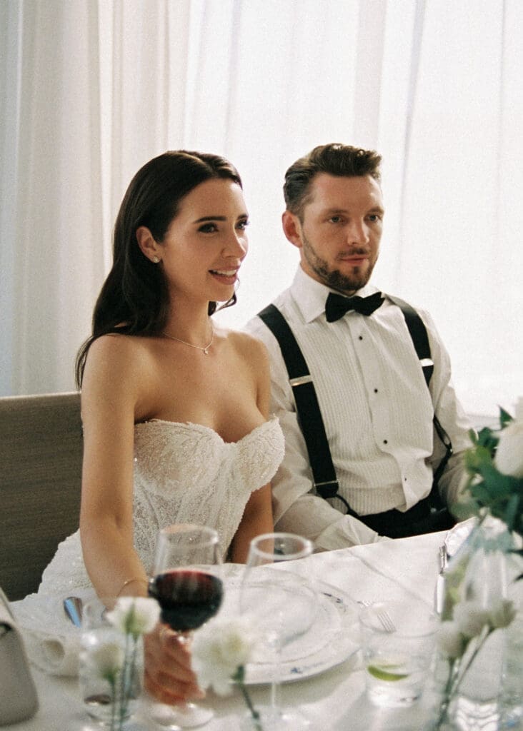 Bride and groom at head table during Kulosaari Casino Helsinki wedding reception, suspenders and red wine, film photography, Miss Moody Photography — Morsian ja sulhanen kunniapöydässä Kulosaaren Casinon häävastaanoton aikana Helsingissä, henkselit ja punaviini, filmivalokuvaus, Miss Moody Photography