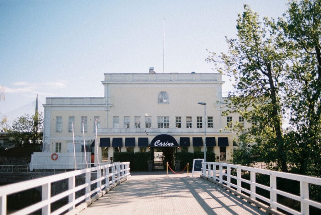 Kulosaari Casino Helsinki wedding venue entrance from boardwalk, navy awnings and Casino sign, film photography, Miss Moody Photography — Kulosaaren Casinon Helsingin häävenueen sisäänkäynti laituriltä, laivastosiniset markiisit ja Casino-kyltti, filmivalokuvaus, Miss Moody Photography