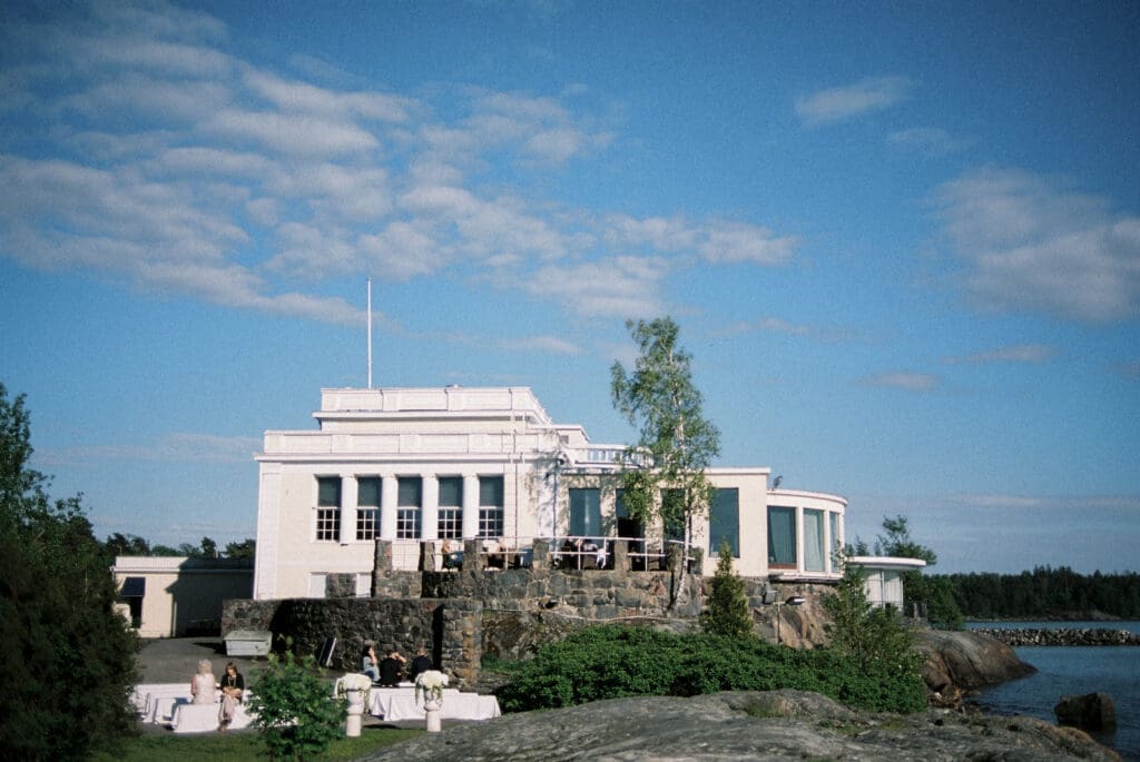 Kulosaari Casino Helsinki wedding venue exterior on rocky island with birch tree and blue sky, film photography, Miss Moody Photography — Kulosaaren Casinon Helsingin häävenueen ulkopuoli kalliosaarella koivupuun ja sinisen taivaan kanssa, filmivalokuvaus, Miss Moody Photography