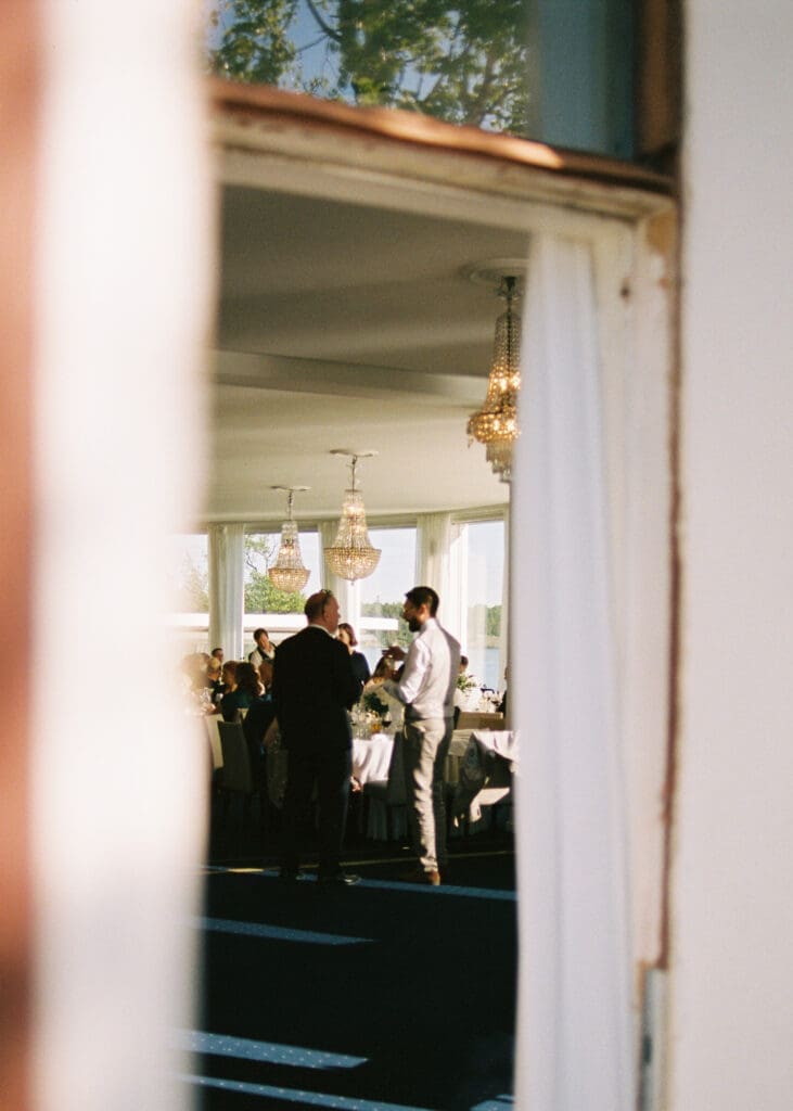 Kulosaari Casino Helsinki wedding reception viewed through doorway with crystal chandeliers, guests mingling, film photography, Miss Moody Photography — Kulosaaren Casinon Helsingin häävastaaanotto ovesta katsottuna kristallikruunuineen, vieraat seurustelevat, filmivalokuvaus, Miss Moody Photography