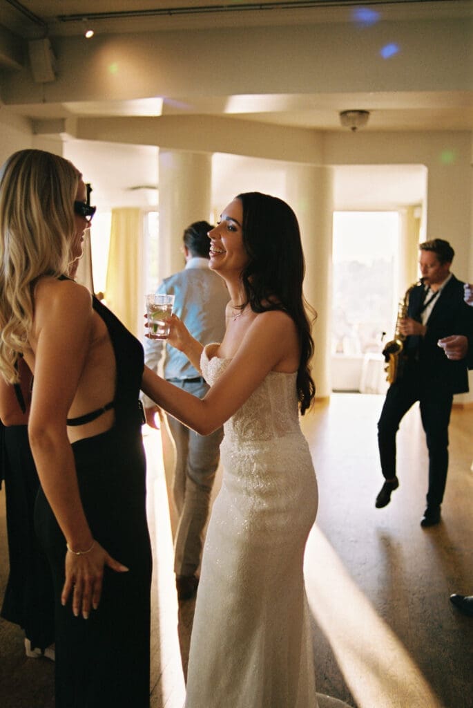 Bride laughing with guest on dance floor at Kulosaari Casino Helsinki wedding reception, saxophone player behind them, film photography, Miss Moody Photography — Morsian nauraa vieraan kanssa tanssilattialla Kulosaaren Casinon häävastaanottolla Helsingissä, saksofonisti heidän takanaan, filmivalokuvaus, Miss Moody Photography