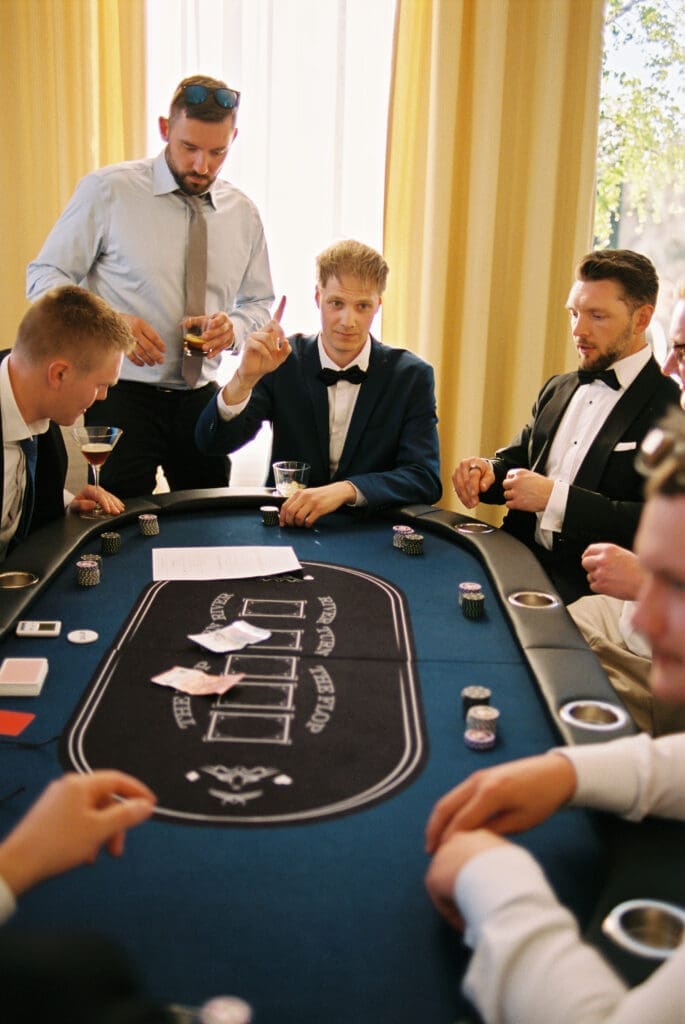 Groomsmen playing poker at wedding reception Kulosaari Casino Helsinki, dealer standing over table, film photography, Miss Moody Photography — Sulhasen kaverit pelaavat pokeria häävastaanottolla Kulosaaren Casinolla Helsingissä, jakaja seisoo pöydän yli, filmivalokuvaus, Miss Moody Photography