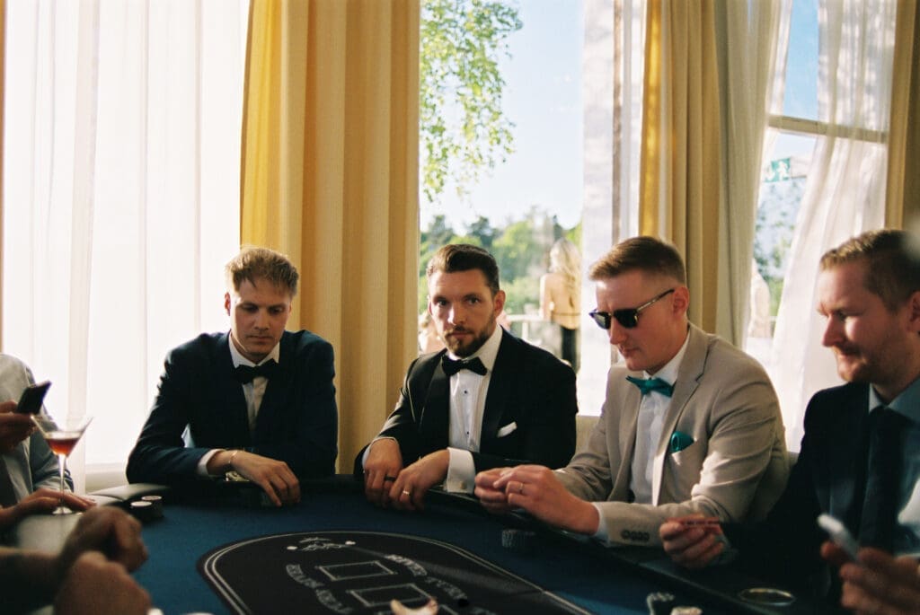 Groomsmen playing poker at wedding reception Kulosaari Casino Helsinki, tuxedos and sunglasses, film photography, Miss Moody Photography — Sulhasen kaverit pelaavat pokeria häävastaanottolla Kulosaaren Casinolla Helsingissä, smokingit ja aurinkolasit, filmivalokuvaus, Miss Moody Photography