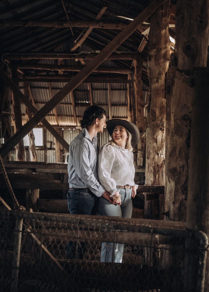 Couple laughing and holding hands inside an old timber farm shed