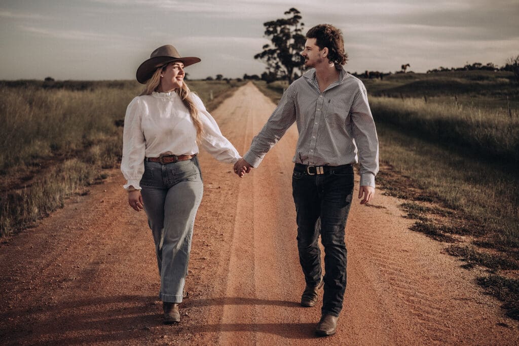 Couple holding hands and walking down a red dirt farm road in Donald, Victoria